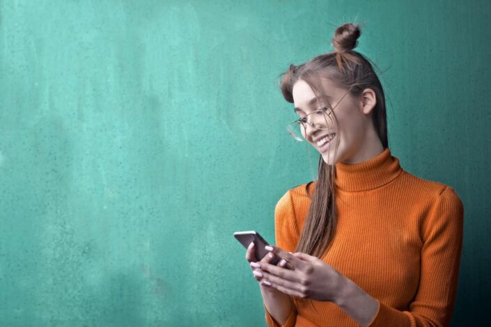 Woman in orange turtleneck sweater holding smartphone