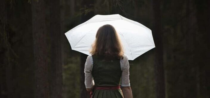 Woman holding umbrella standing on tree stump