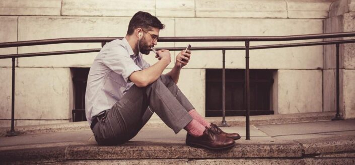 a man sitting on the pavement, using his phone